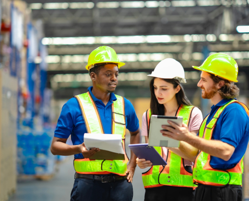 Workers In Hardhats In Warehouse Ooking At Data